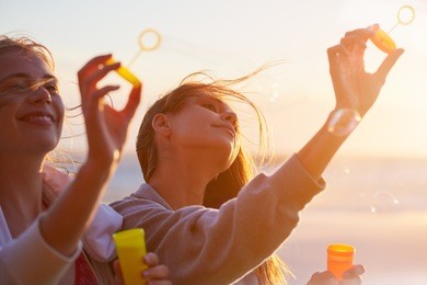 pretty teenage girls at sunset blow bubbles holding hands out with warm lens flare shining through