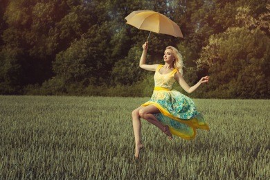 girl levitates over the green field on the umbrella. she is wearing a nice summer dress.