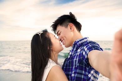 couple taking self portrait photos with smart phone on the beach