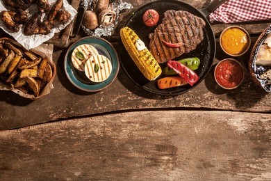 high angle view of grilled meal of steak, chicken and vegetables spread out on rustic wooden table at barbeque party