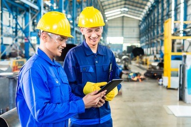 two workers in production plant as team discussing, industrial scene in background