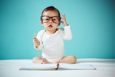 asian baby writing in a book and sitting on the bed in the blue bedroom, baby healthy and preschool concept