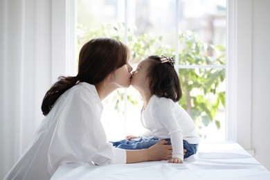 beautiful asian mom and her cute daughter kissing with love while looking at each other

