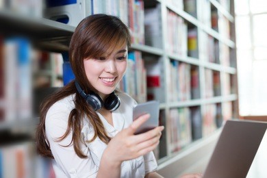 asian beautiful female student using laptop and mobile phone in library