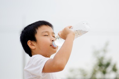 asian young boy drinking fresh water from plastic bottle after sport in daylight