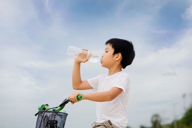 asian young boy sit on bicycle  drinking fresh water from plastic bottle after sport in daylight