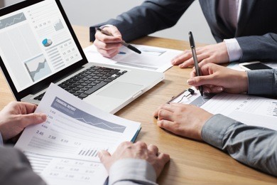 business professionals working together at office desk, hands close up pointing out financial data on a report, teamwork concept