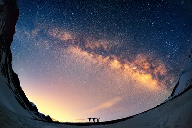 silhouettes of the people standing together holding hands against the milky way in the mountains. 