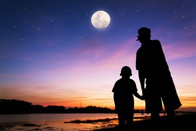silhouette of father and son point look at to  full moon after sunset at  the river background