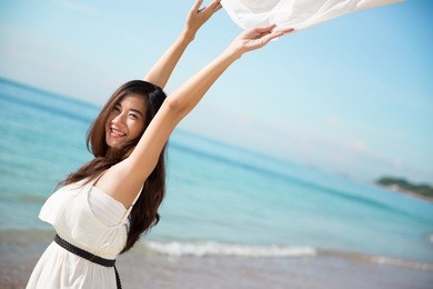 a portrait of an asian woman enjoying her time in the beach, closing her eyes and arms open wide