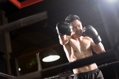 young athletic man with boxing gloves on boxing ring. lens flare