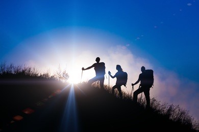 people meeting sunrise team building session. group of people silhouettes walking toward mountain summit with backpacks hiking trekking gear meeting uprising sun sunbeams and blue sky of background
