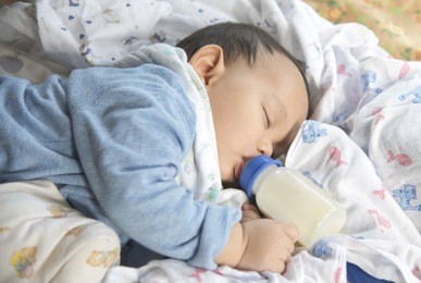 cute and adorable asian baby sleeping and drinking milk from the bottle alone on the bed