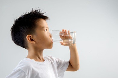 asian young boy in white shirt hold glass of fresh water in hand and drink. concept water day.