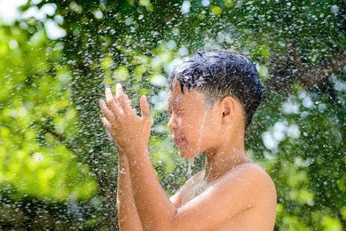 asian boy washing face and hair from fresh water outside home under the daylight green bokeh from green tree