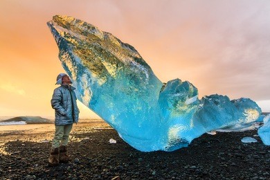 extremely beautiful young man posing next to a very big chunk of beached ice near jokulsarlon, iceland, at sunset