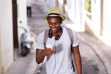 portrait of a happy young african american man walking in town with mobile phone