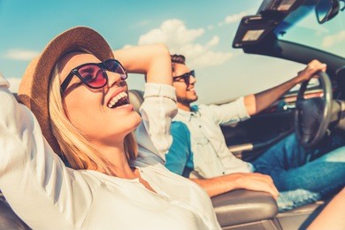 freedom of the open road. side view of joyful young woman relaxing on the front seat while her boyfriend sitting near and driving their convertible 