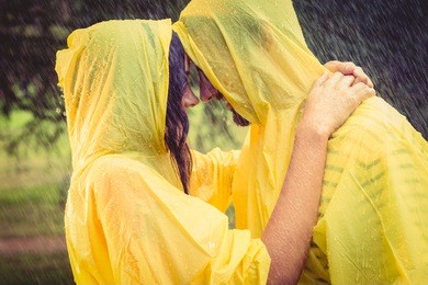 cute couple wearing protection cape and hugging under the rain in the park