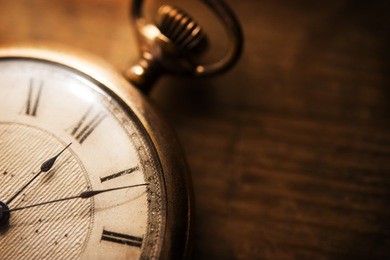 old pocket watch on grungy wooden desk. shot in low key and extremely shallow depth for impressional feel. focus is on etching of clock face plate.