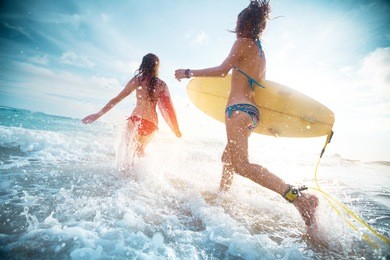 two ladies running into the sea with surf boards
