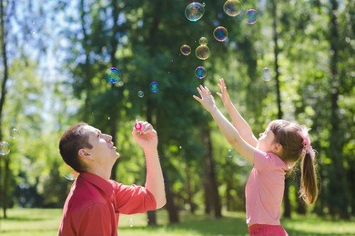 a dad and his daughter are making bubbles in the park