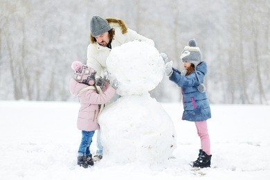 young father and his two daughters building a snowman on winter day