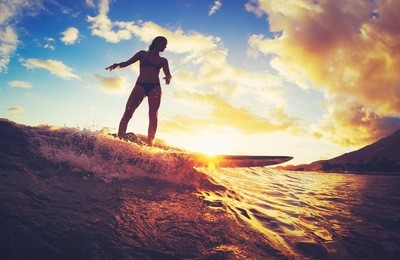 surfing at sunset. beautiful young woman riding wave at sunset. outdoor active lifestyle.
