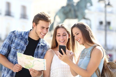 three tourist friends consulting gps on smart phone in a touristic place with a monument in the background