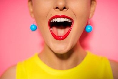 scream and shout! close up of opened female mouth. bright red lips. pink background