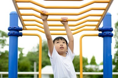 young asian boy hang the yellow bar by his hand to exercise at out door playground