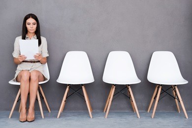 waiting for interview. confident young businesswoman holding paper while sitting on chair against grey background