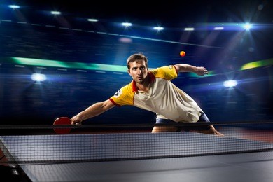 young sports man tennis player is playing on black background with lights