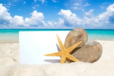 large wooden heart, stafish and a postcard with copy space on the sunny beach