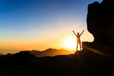 woman successful hiking climbing silhouette in mountains, motivation and inspiration in beautiful sunset and ocean. climber arms up outstretched on mountain top looking at inspirational landscape.