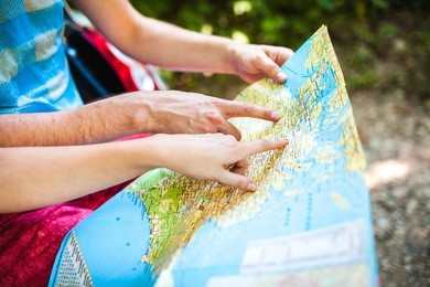 hands closeup of a young traveler looking at a map while sitting in car trunk