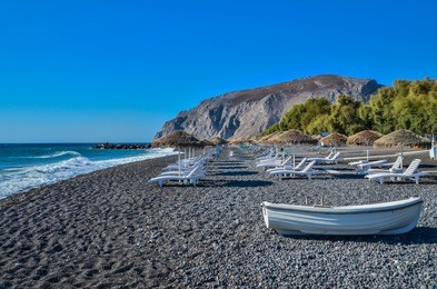 boat and tanning beds with umbrellas at kamari beach, santorini, greece