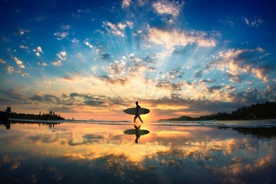 sun surfer. a man is walking with a surf in his hands across the sea shore. 