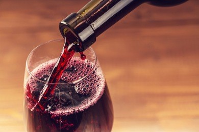 pouring red wine into the glass against wooden background