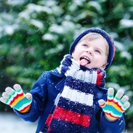 cute little funny child in colorful winter clothes having fun with snow, outdoors during snowfall. active outdoors leisure with children in winter. kid with  hat, hand gloves with stripes.