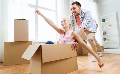 home, people, moving and real estate concept - happy couple having fun and riding in cardboard boxes at new home
