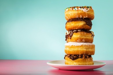 stack of assorted donuts on a white plate on pastel blue and pink background