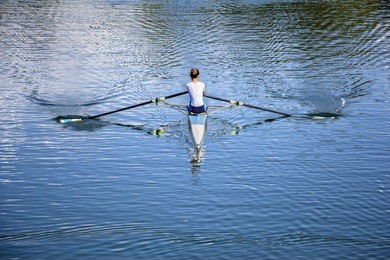 women rower in a boat, rowing on the tranquil lake