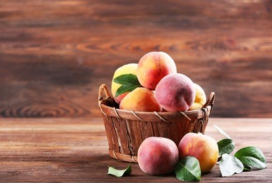 fresh peaches in wicker basket on wooden background