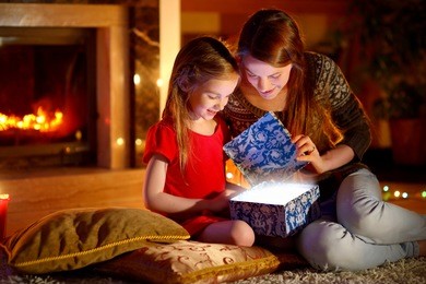 young mother and her little daughter opening a magical christmas gift by a christmas tree in cozy living room in winter