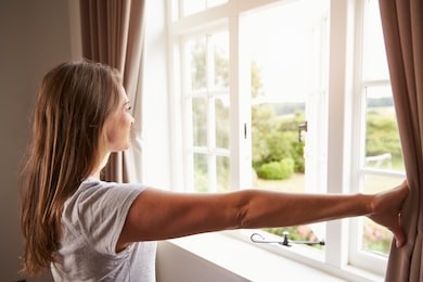 woman standing by bedroom window and opening curtains