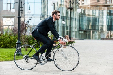 going everywhere by his bike. side view of young businessman looking forward while riding on his bicycle