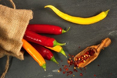 multicolored hot peppers spilling from burlap bag with scoop of hot pepper flakes