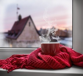 cup with a hot drink on the windowsill in the background of a winter city. focus on the edge of the cup