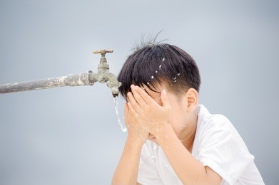 young asian boy use water from old faucet to wash his face and hair on grey cloud on the sky before rain.
